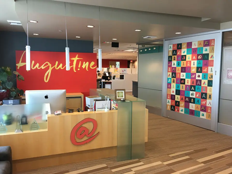 Reception area with a red Augustine wall sign and a logo on the front desk