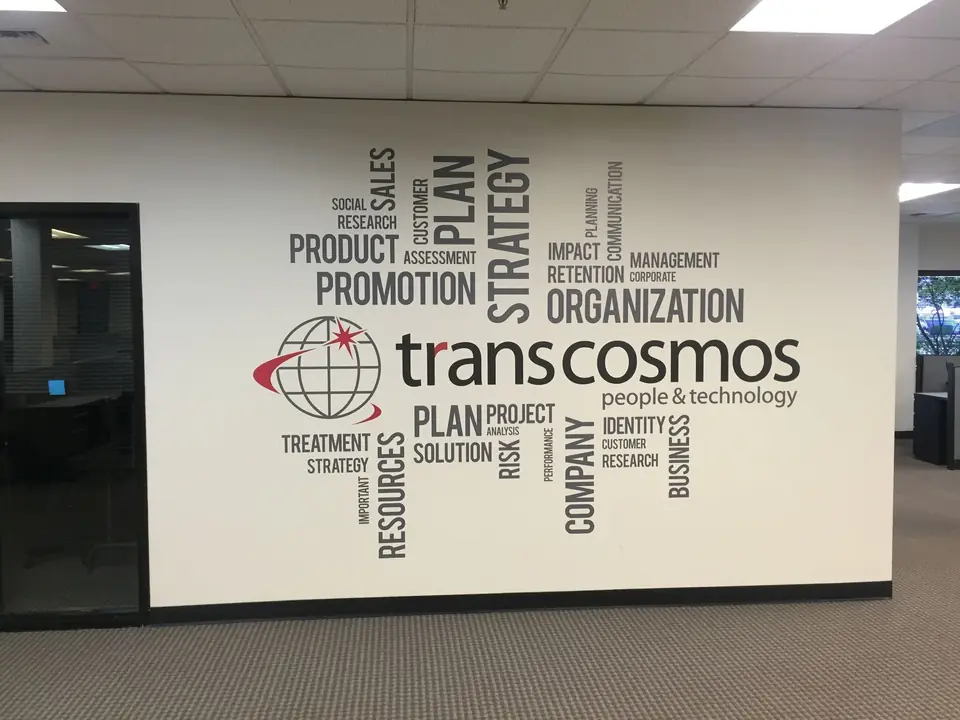 Word-cloud wall graphic with the transcosmos logo in an office